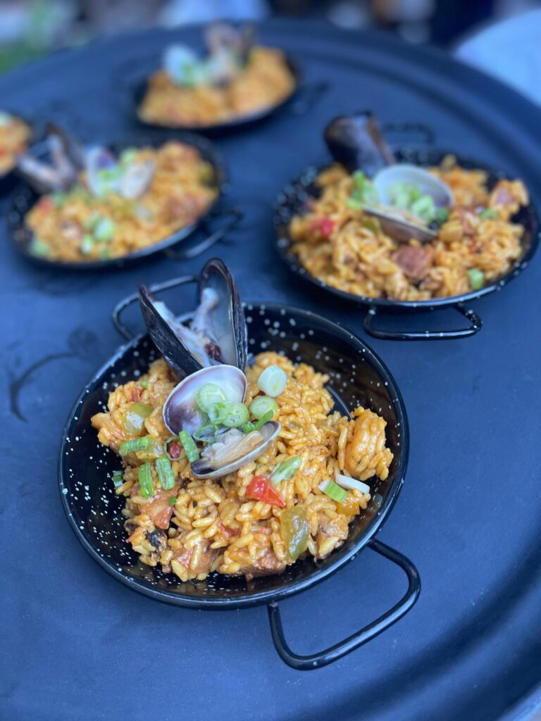 Individual servings of Spanish paella in traditional steel pans at a PSRT Bay Area holiday event